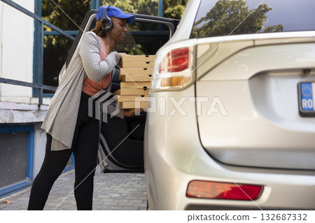 African american urban courier with massive pile of pizza boxes, delivering fast food order from a restaurant. Driving the courier service car to bring bigger meal orders, pizza delivery. 132687332