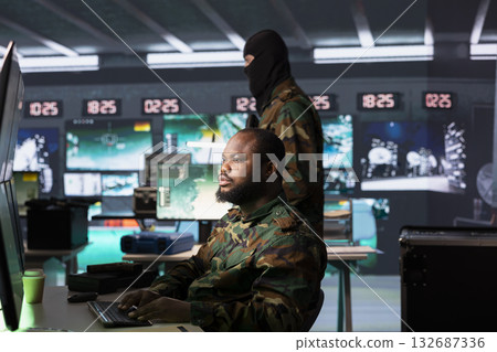 Military operative conducts tactical surveillance, utilizing hardware for data analysis and mission planning. African american air defense agent looks at aerial map on screen, pinpointing targets Military operative conducts tactical surveillance, utilizing hardware for data analysis and mission planning. African american air defense agent looks at aerial map on screen, pinpointing targets 132687336