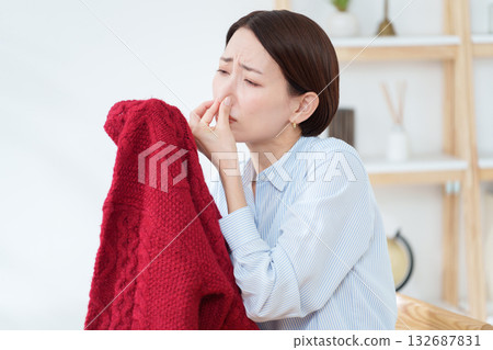 一位女士正在聞她拿出來準備換穿的毛衣。 一位女士正在聞她拿出來準備換穿的毛衣。 132687831