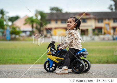 toddler girl riding an electric motorcycle toy in park 132688918