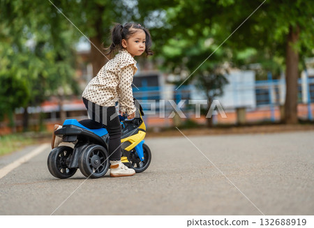 toddler girl riding an electric motorcycle toy in park toddler girl riding an electric motorcycle toy in park 132688919