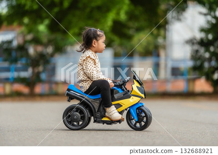 toddler girl riding an electric motorcycle toy in park 132688921