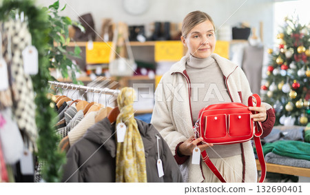 adult woman chooses fashionable handbags in a store against the background of a Christmas tree adult woman chooses fashionable handbags in a store against the background of a Christmas tree 132690401