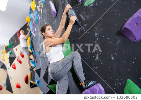 Young woman climbs steep artificial wall in sports complex and trains endurance Young woman climbs steep artificial wall in sports complex and trains endurance 132690502