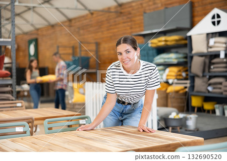 Interested girl choosing comfortable garden table in store 132690520