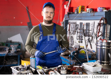 Positive male worker of car workshop holding metal tool in car workshop Positive male worker of car workshop holding metal tool in car workshop 132690522