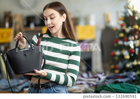 Positive young woman choosing handbag in clothing store Positive young woman choosing handbag in clothing store 132690591