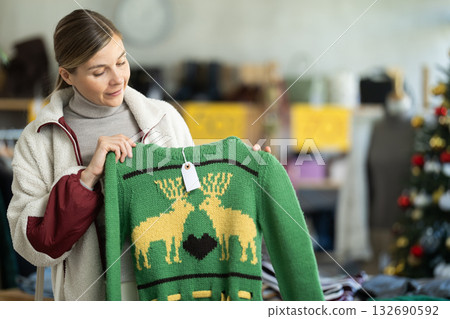 Positive young woman choosing sweater in clothing store 132690592