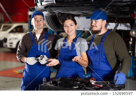 Portrait of professional auto mechanics in auto repair shop next to car on lift 132690597