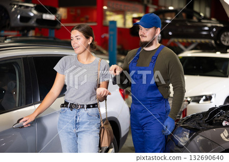 Young male mechanic giving car keys to woman client Young male mechanic giving car keys to woman client 132690640