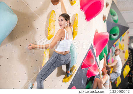 Young woman climbs steep artificial wall in sports complex and trains endurance Young woman climbs steep artificial wall in sports complex and trains endurance 132690642