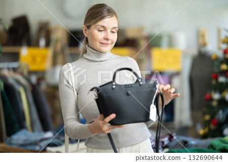 Positive young woman choosing handbag in clothing store 132690644