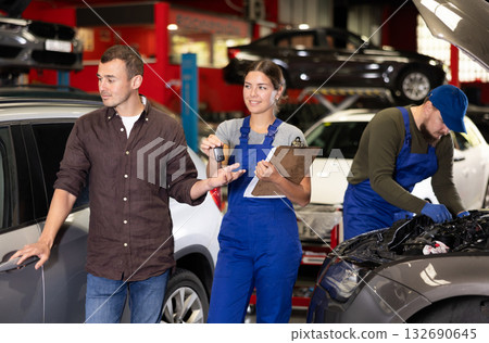 Polite female worker of auto shop giving the keys of car to male client 132690645