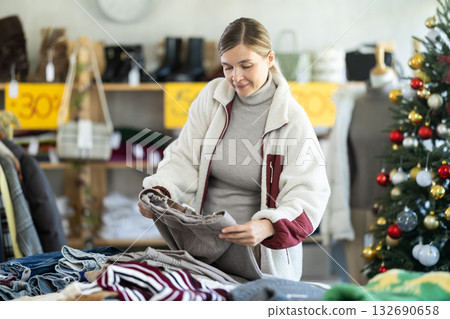 Woman client looks at products in store, choose closely ladys trousers 132690658