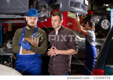 Male worker of auto service speaking to man client concerning his notes on paper 132690759