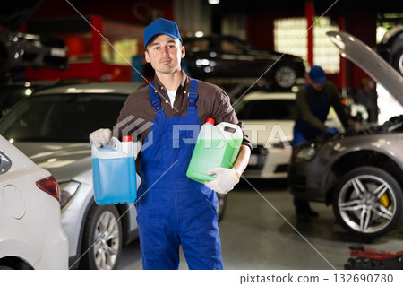 Positive male worker of car workshop holding full plastic cans Positive male worker of car workshop holding full plastic cans 132690780