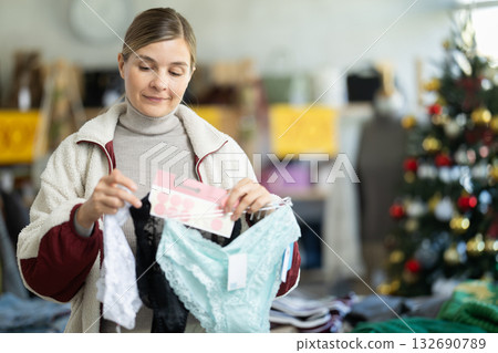 Young woman choosing panty sets on Christmas tree background in clothing store Young woman choosing panty sets on Christmas tree background in clothing store 132690789