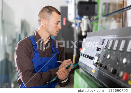 Technician writing on clipboard while operating industrial machinery 132690795