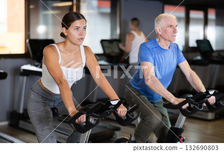 Concentrated young girl working out on stationary bicycle in gym. Healthy active lifestyle concept Concentrated young girl working out on stationary bicycle in gym. Healthy active lifestyle concept 132690803