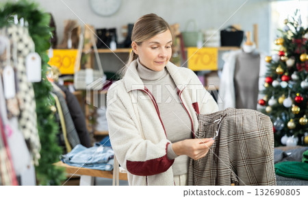 Woman client looks at products in store, choose closely ladys trousers Woman client looks at products in store, choose closely ladys trousers 132690805