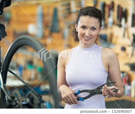 Portrait of young female master posing with tool, prepared for repair bicycle in workshop 132690807