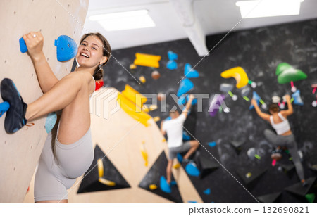 Young woman climbs steep artificial wall in sports complex and trains endurance 132690821