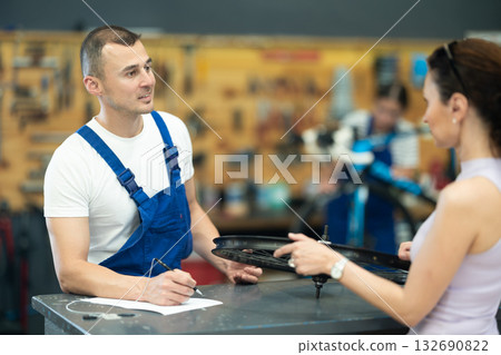 Young experienced man seller taking order and talking with woman client about bicycle in workshop Young experienced man seller taking order and talking with woman client about bicycle in workshop 132690822