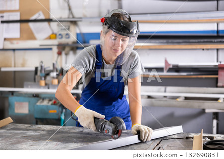 Workwoman cutting plastic profile with angle grinder in workshop 132690831
