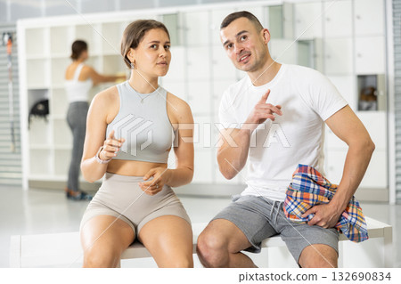 Young woman and man sitting, exchanged couple of phrases in locker room after changing clothes Young woman and man sitting, exchanged couple of phrases in locker room after changing clothes 132690834