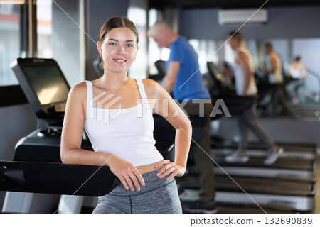 Young woman posing by treadmill in gym Young woman posing by treadmill in gym 132690839