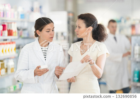 Female pharmacist helping woman with prescription choosing medical supplies at drugstore 132690856