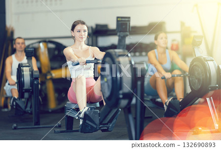 Athletic woman in sportswear training on rowing machine in sport gym Athletic woman in sportswear training on rowing machine in sport gym 132690893