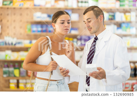 Male pharmacist consulting young girl about medicament in box Male pharmacist consulting young girl about medicament in box 132690985