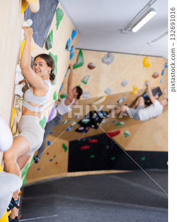 Smiling young female climber conquering bouldering wall at gym Smiling young female climber conquering bouldering wall at gym 132691016