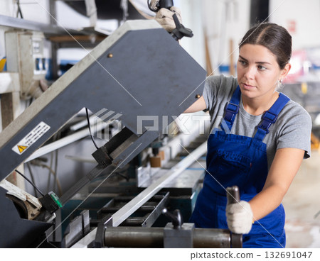 Glass workshop - girl works on machine for cutting aluminum profiles for windows 132691047