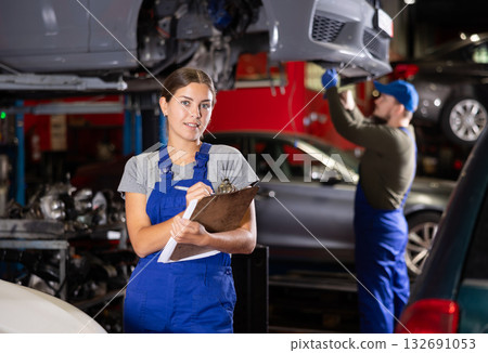 Smiling female worker of auto service welcoming clients holding sheets of paper 132691053