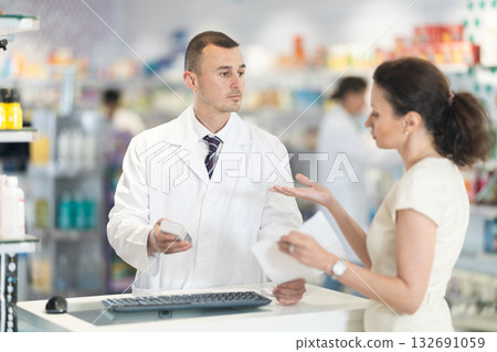 Male pharmacist consulting woman client about medicament in box according to recipe Male pharmacist consulting woman client about medicament in box according to recipe 132691059
