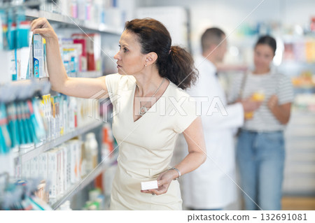 Woman buyer carefully chooses a medicine in pharmacy Woman buyer carefully chooses a medicine in pharmacy 132691081