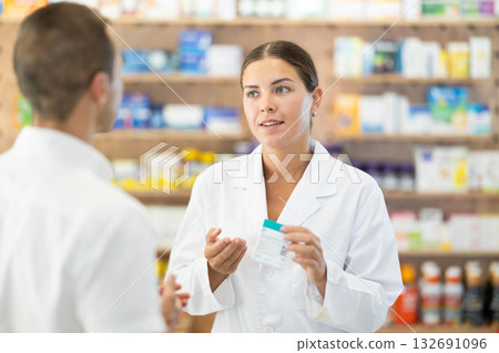 Female pharmacist consulting young guy about medicament in box Female pharmacist consulting young guy about medicament in box 132691096