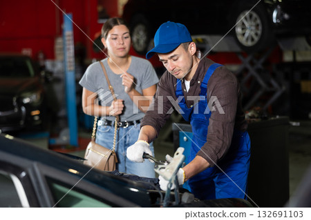 Skilled male auto mechanic controlling automobile detail while young girl looking at it disappointedly 132691103