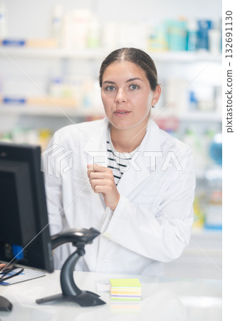 Young female pharmacist standing at monitor in chemist's shop Young female pharmacist standing at monitor in chemist's shop 132691130