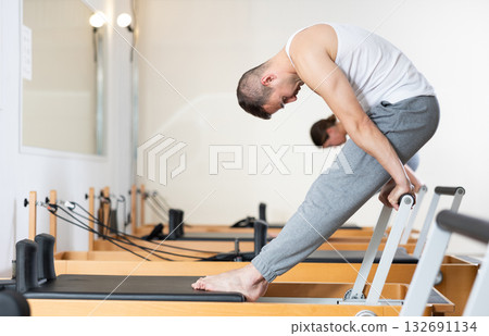 Man performing pilates exercises on reformer at group workout 132691134