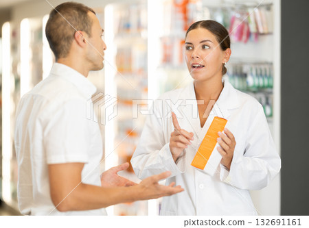 Female consultant pharmacist holds cream in hands and offers man client to purchase Female consultant pharmacist holds cream in hands and offers man client to purchase 132691161