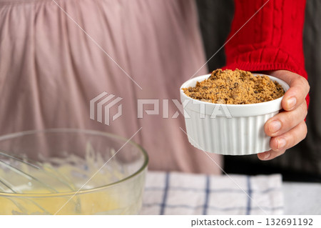 Close-up of a person holding a ramekin filled with brown sugar, ready for holiday cookie baking Close-up of a person holding a ramekin filled with brown sugar, ready for holiday cookie baking 132691192