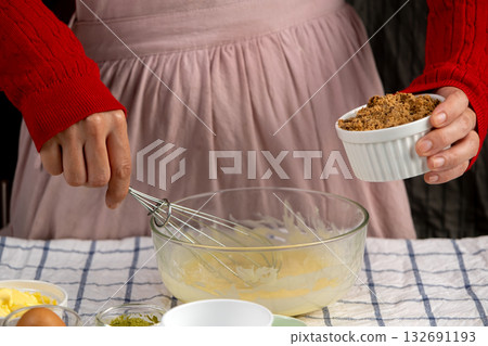 Hands preparing to mix brown sugar into a bowl of creamed butter and eggs, perfect for holiday cookie baking 132691193