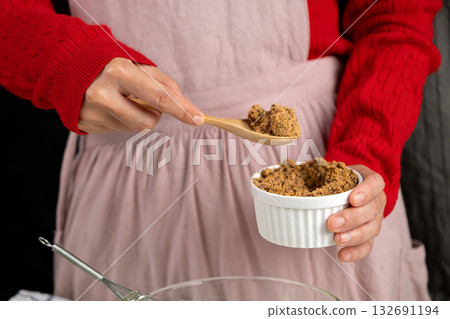 Hand scooping brown sugar with a wooden spoon, ready for holiday cookie baking. Warm and cozy kitchen moment 132691194