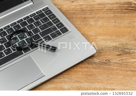 Close-up of a laptop keyboard with a magnifying glass resting on it Close-up of a laptop keyboard with a magnifying glass resting on it 132691532