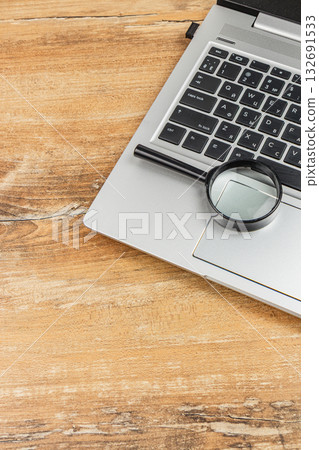 Exploring details with a magnifying glass on a laptop at a wooden desk Exploring details with a magnifying glass on a laptop at a wooden desk 132691533