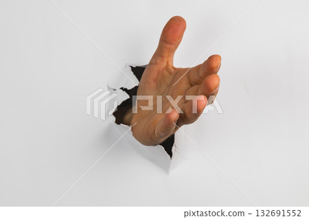 Hand reaching through a hole in a white wall creating a unique visual effect Hand reaching through a hole in a white wall creating a unique visual effect 132691552