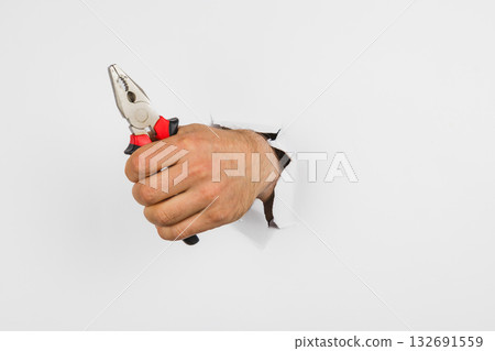 Hand holding pliers reaches through a torn wall in a playful scene 132691559
